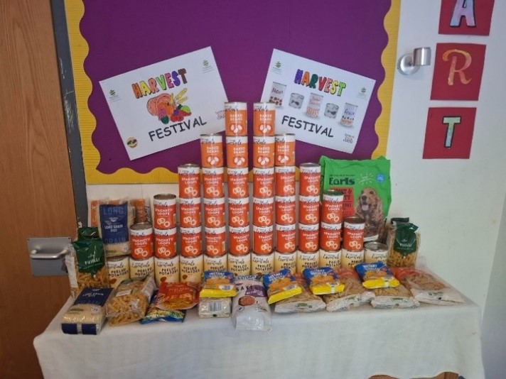 clothed table infront of a purple harvest festival signed wall. the table has pasta, tinned food and dog food.