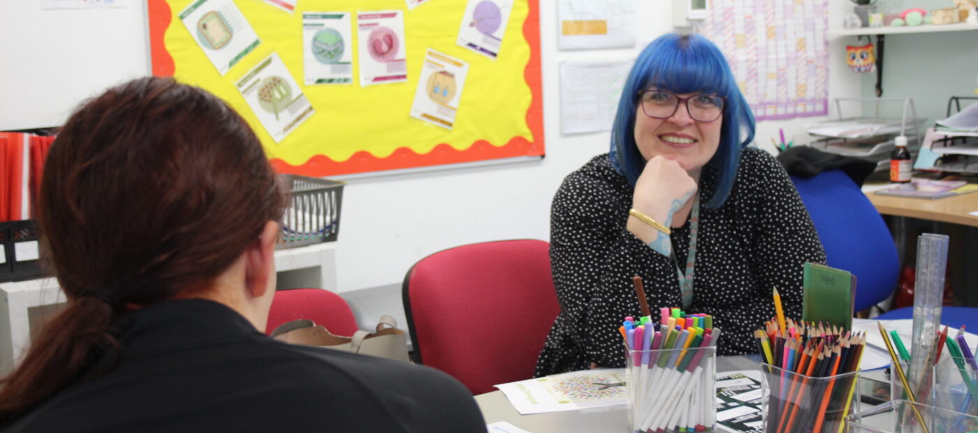 blue haired teacher in a black and white polka dot shirt, in a classroom setting