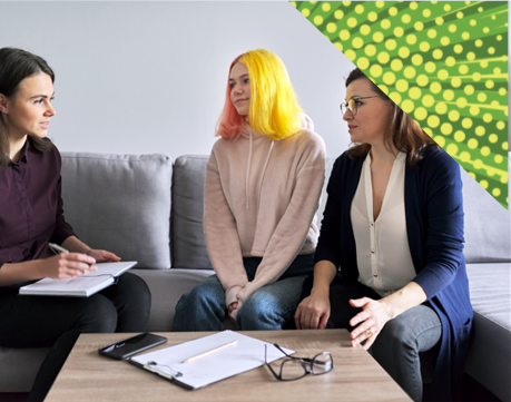 three women sat on a gray sofa talking, one woman is making notes