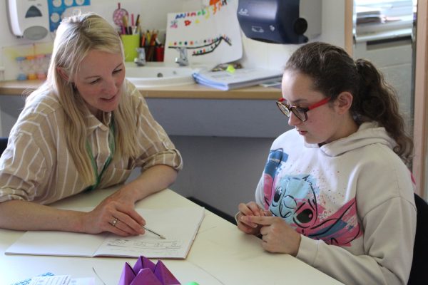 A blonde woman pointing at paper with a pen smiling and a young brunette girl looking at the paper